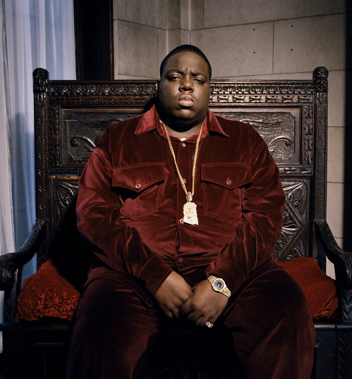 Man in a red velvet outfit sitting on an ornate wooden chair, evoking a mysterious and creepy mood.