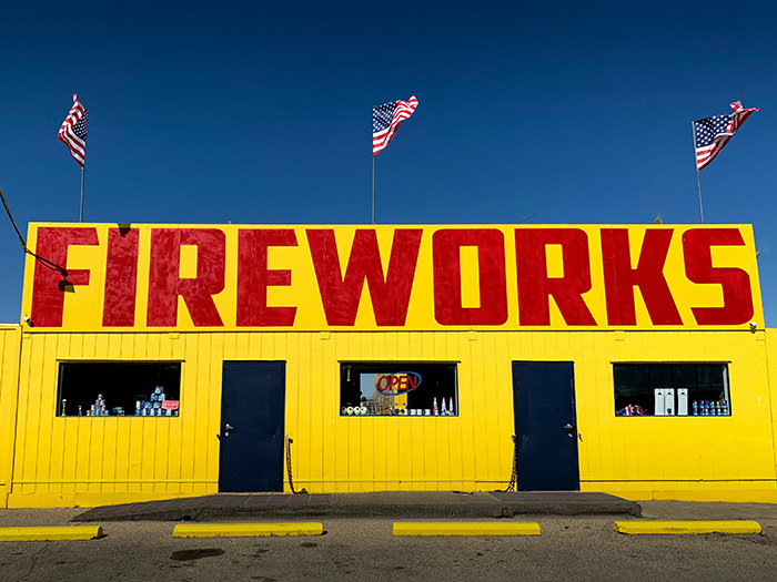 Bright yellow fireworks stand with bold red letters and American flags, symbolizing staff handling rude customers with satisfaction.