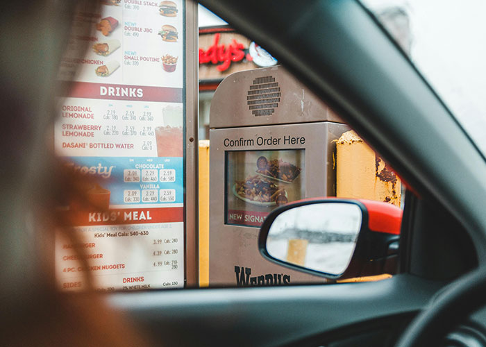 View from inside a car at a fast food drive-thru order menu and speaker, highlighting economy signs in daily life.