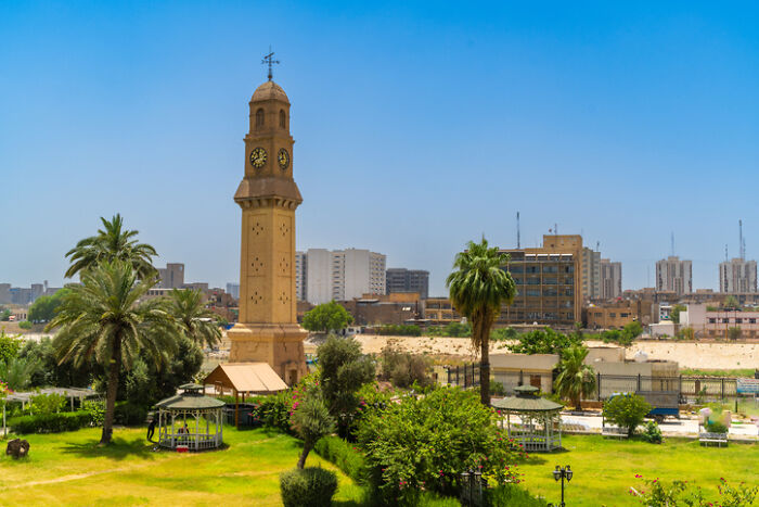 Sunny urban park with a prominent clock tower, palm trees, and city buildings, illustrating Work-Life Balance challenges.