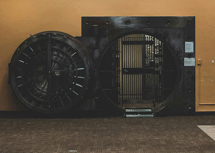 An impressive, heavy bank vault door, half-open, revealing rows of safe deposit boxes inside. Exclusive access to incredible places.