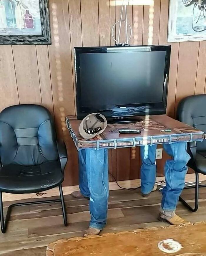 Table with jeans legs as supports holding a TV, a confusing and unhinged image where things only get weirder.