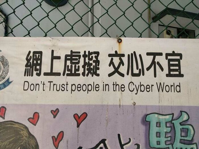 Sign on chain link fence with text warning not to trust people in the cyber world, a confusing and unhinged image.