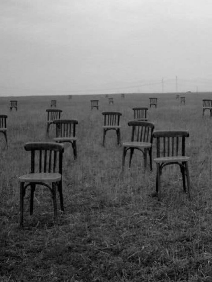 Empty wooden chairs scattered across a foggy field creating a confusing and unhinged visual scene.