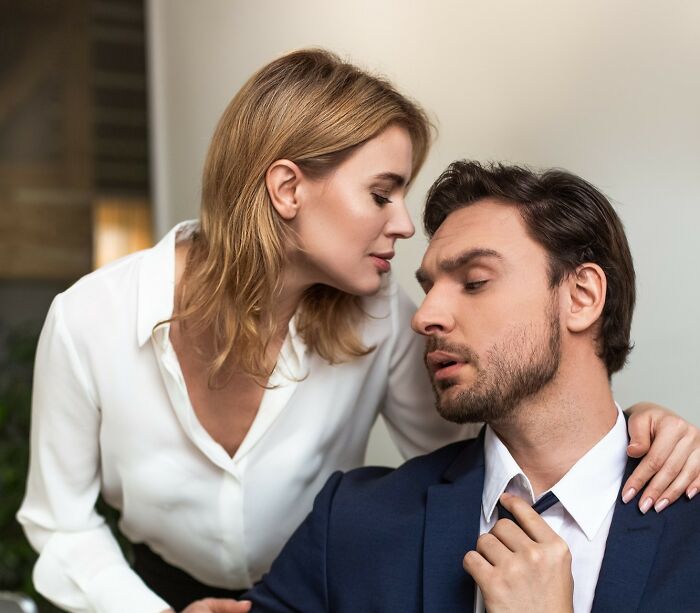 A woman with her hand on a man's shoulder, as he loosens his tie, suggesting a wild rumour.