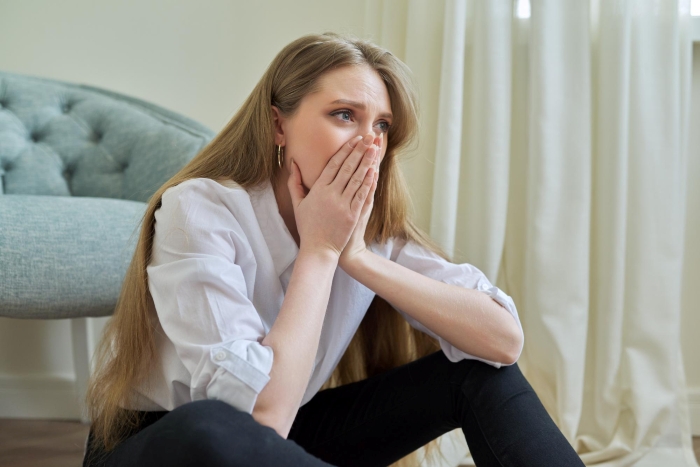 Young woman looking shocked and worried, covering her mouth, reflecting on cheating and scamming consequences at home.