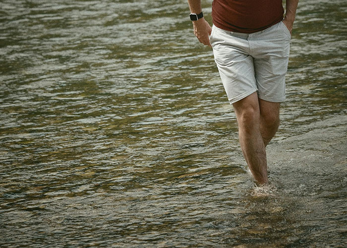 Man wearing shorts and a watch walking barefoot in water, illustrating unexpected dangers in everyday activities.