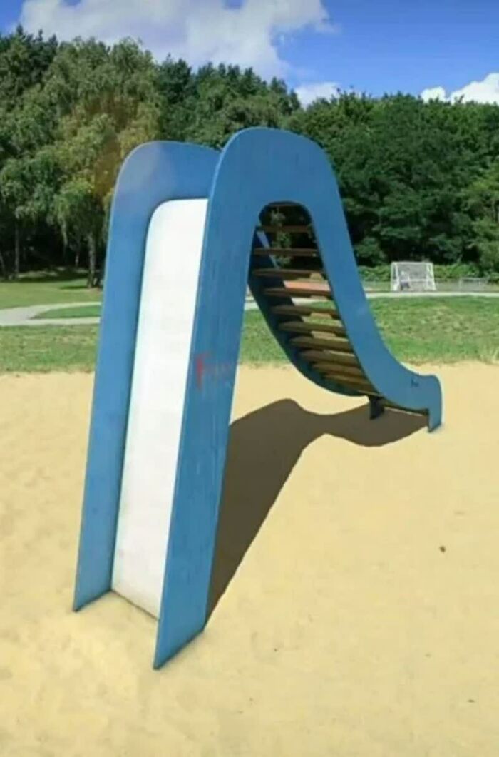 A blue playground slide with a ladder on a sandy surface, looking like a weird image that lives rent-free in your mind.