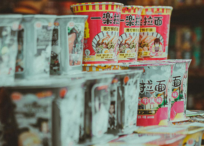Instant noodle cups stacked on shelves in a store, illustrating signs of economy not doing well.