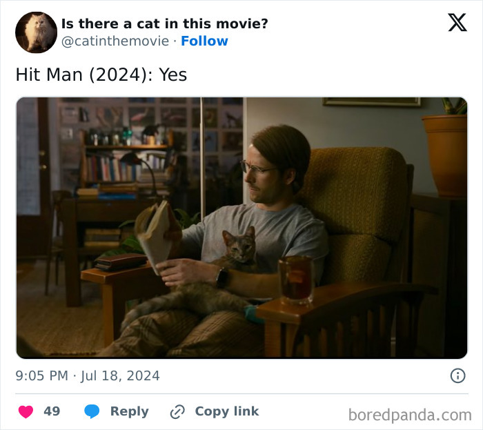 A man reading a book in a chair, a cat in cinema on his lap, with a drink on the side table.