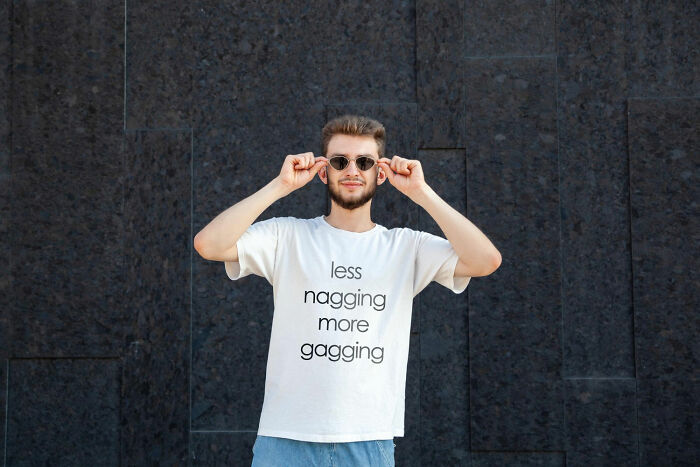 Young man wearing sunglasses and a white shirt with text, posing confidently against a dark wall, symbolizing future breakup stories.