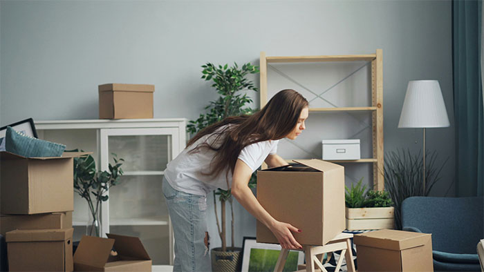 Woman lifting a moving box in a room filled with packed boxes, capturing a moment in a dramatic family story.