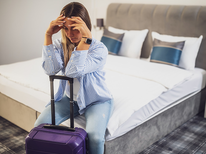 A frustrated woman sitting on a suitcase in a hotel room, depicting rude customers learning not to mess with staff.