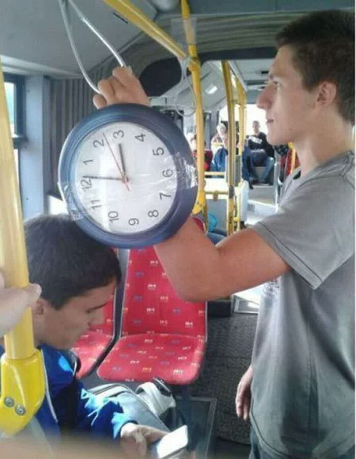 A man holding a wall clock by the bus handle, making a weird image that lives rent-free in your mind.