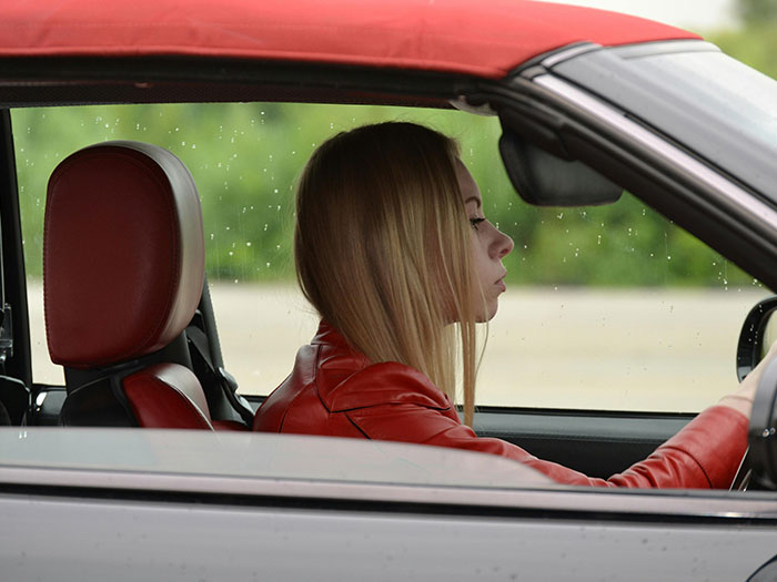 A young woman with blonde hair, wearing a red leather jacket, looking pensive while driving. Could this be a bad first date?