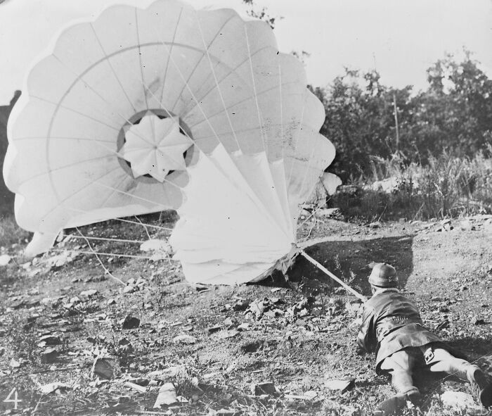 Soldier retrieving a parachute on a rugged landscape in a rare and interesting photo from a time we will never experience.