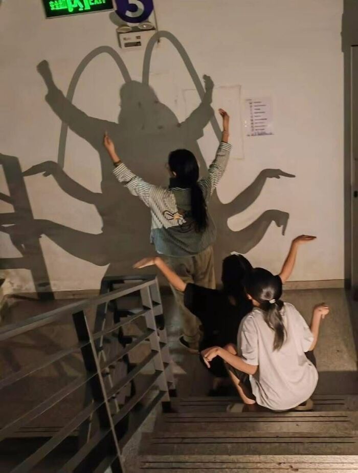 Three people posing on stairs to create a creative shadow with multiple arms on the wall, showcasing hilarious poses.