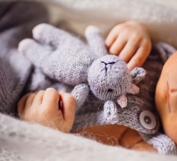 Close de um bebê segurando um brinquedo de malha, relacionado ao desejo da mulher de adotar o bebê por seu irmão.