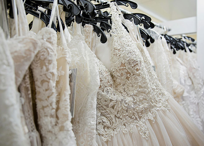 Close-up of intricate wedding dresses hanging on black hangers in a bridal shop, highlighting detailed lace and embroidery.