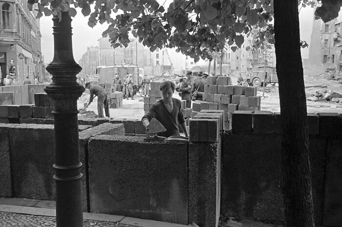 Black and white photo of workers building a concrete block wall, illustrating historical events from 1960 to 2010 by year.