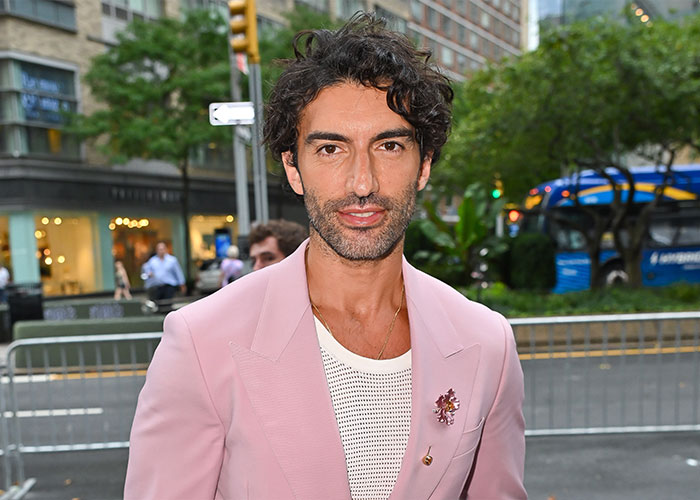 Homem de blazer rosa e camisa de malha branca ao ar livre, relacionado à violenta batalha legal de Blake Lively com Justin Baldoni.