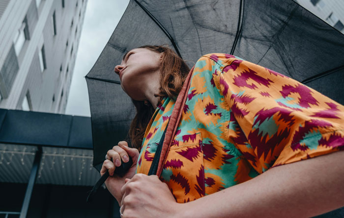 Young woman in colorful patterned shirt holding a black umbrella looking up outdoors capturing unhinged ways women make men uncomfortable