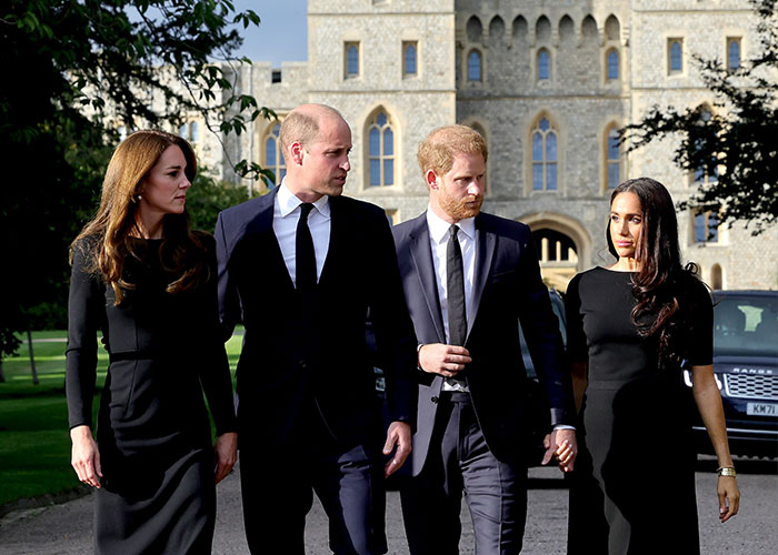 Prince Harry and Meghan Markle walking with Prince William and Kate Middleton outside a historic castle on a sunny day.