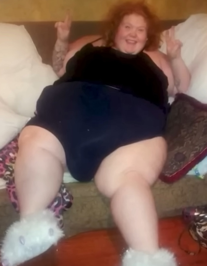 My 600-Lb Life star Dolly Martinez sitting on a couch, smiling and making peace signs with her hands.