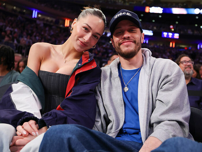 Pete Davidson sitting with a woman at an event, sparking debate about adult content and fatherhood.