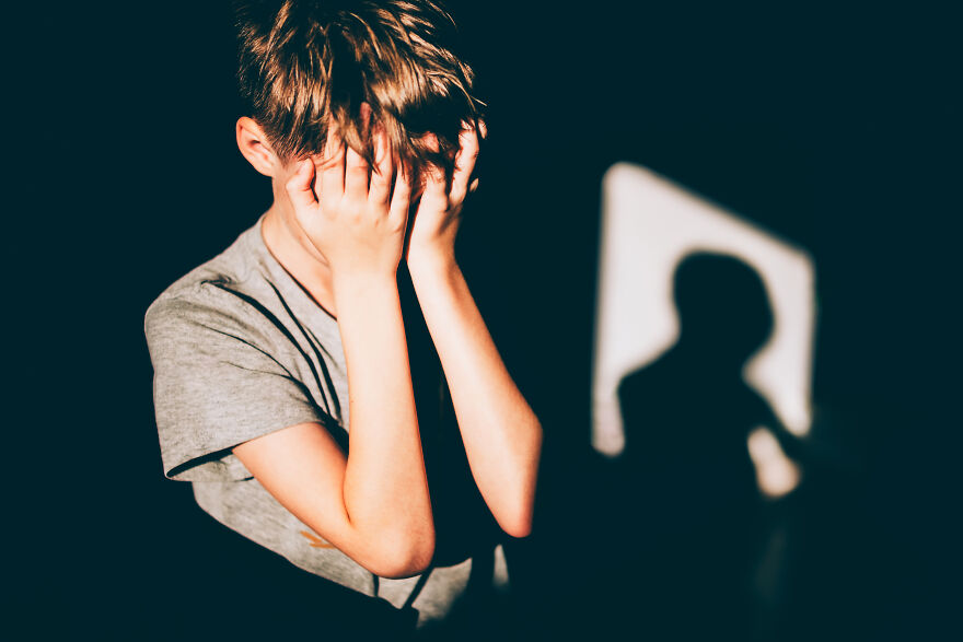 Young boy covering face with hands in a dark room, illustrating the golden child syndrome and its hidden struggles.