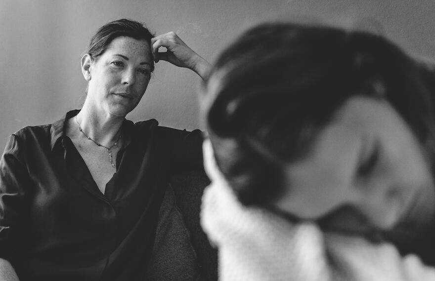 Sad child looking down while woman in the background watches thoughtfully, illustrating scapegoat child family dynamics.