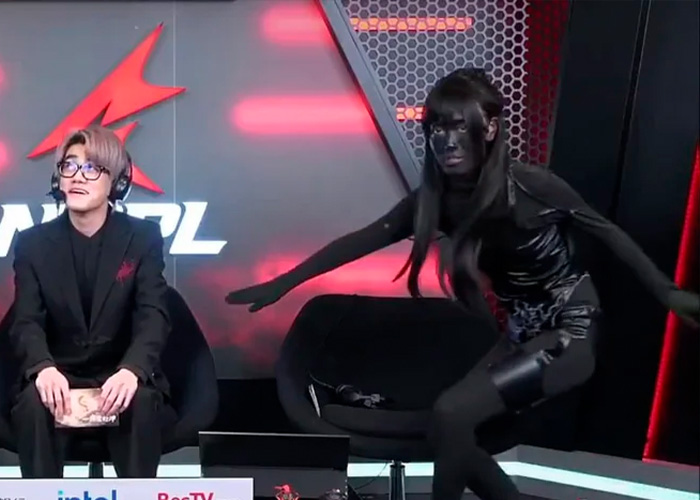 Esports hosts on stage with one in a revealing outfit responding to trolls during a live event broadcast. Esports hosts on stage with one in a revealing outfit responding to trolls during a live event broadcast.