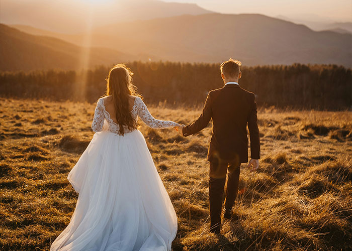 Bride-to-be and fianc&eacute; walking hand in hand in a field at sunset, highlighting devastated bride-to-be exposed fianc&eacute; crimes.