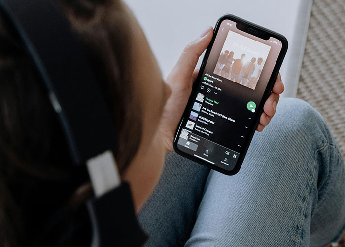 Person wearing headphones and holding a smartphone, browsing signs related to the economy’s current state.
