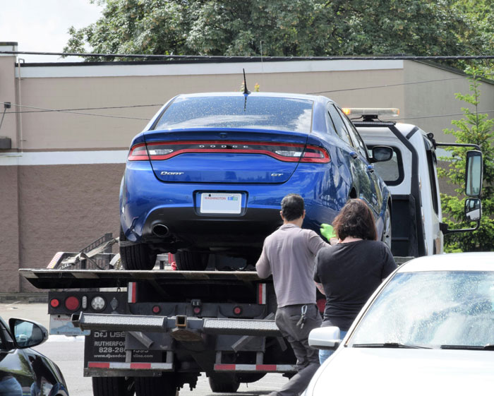 A blue Dodge Dart being loaded onto a tow truck. Shows why people think the person they are dating was dumb.