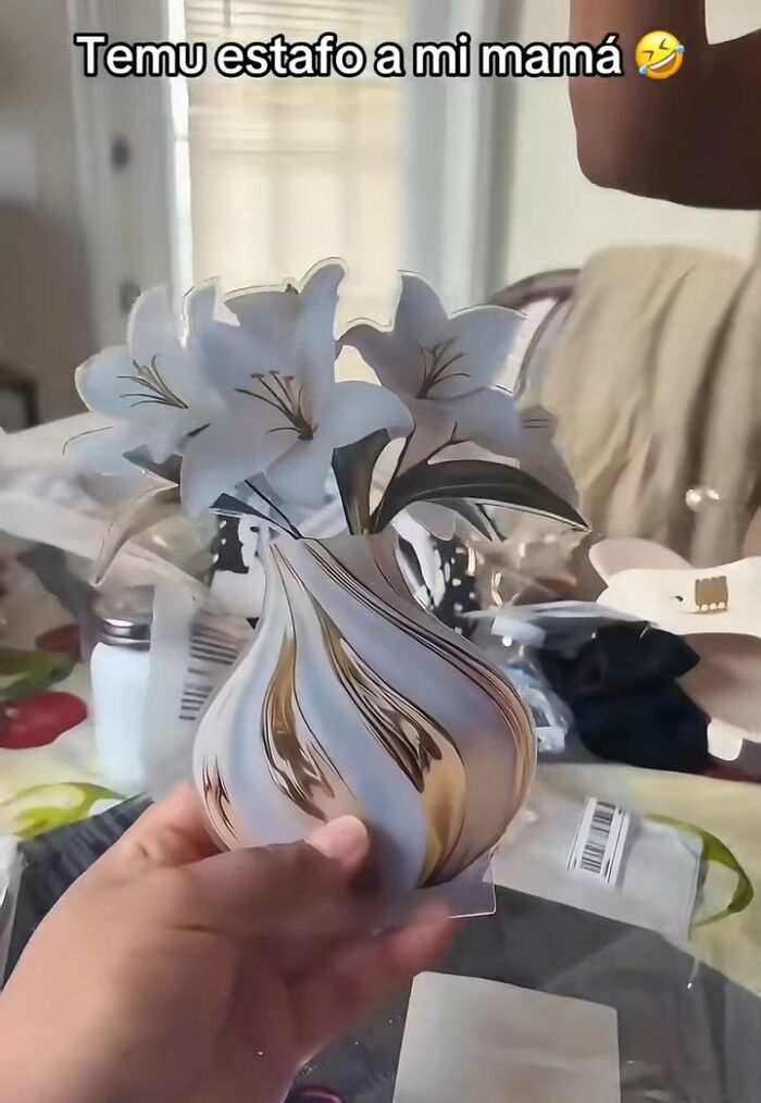Hand holding a flat paper vase with white flowers, showing a funny lesson from people ordering something from Temu.
