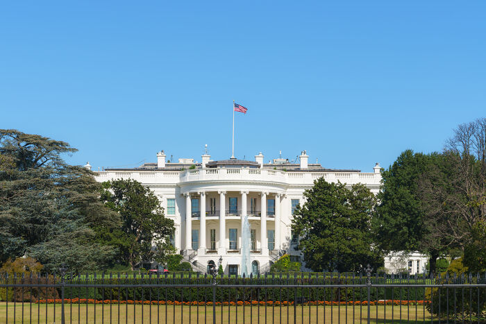 White House with an American flag, fountain, and green lawn. Reflects on work-life balance for countries.