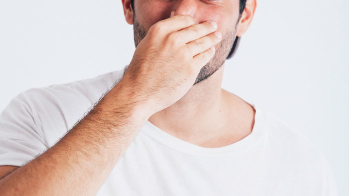 A man in a white shirt covers his nose with his hand, showing disgust at a gross office story or shared workspace.