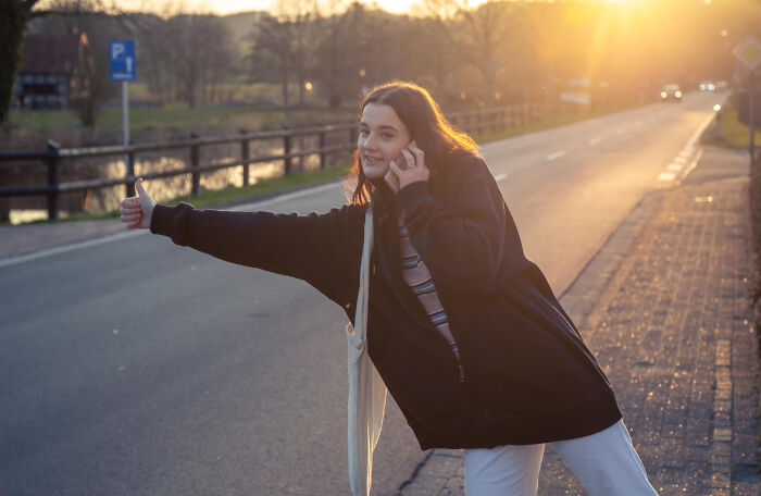 Young person hitchhiking on a rural road at sunset, illustrating kids with no survival instincts stories.