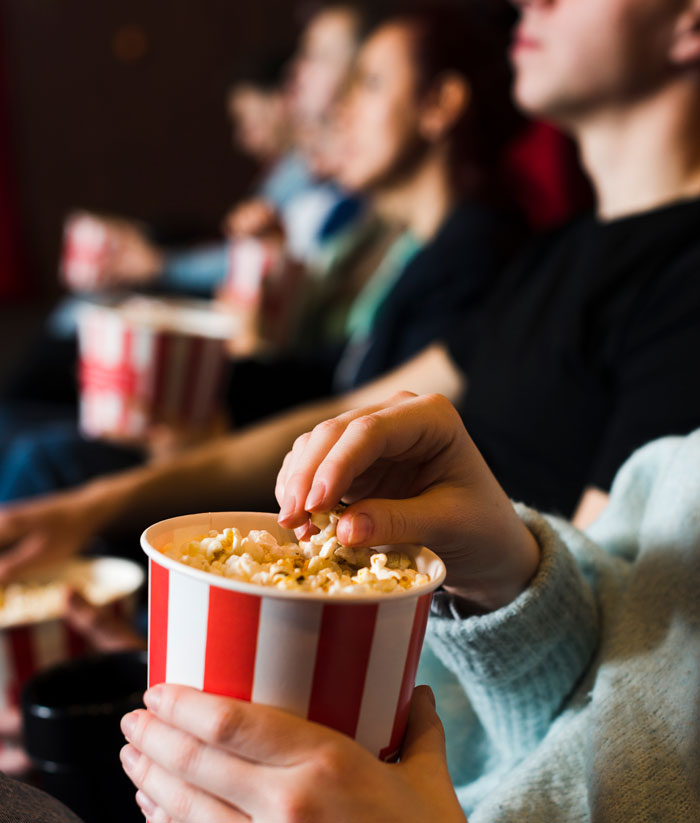 Family at the movies sharing popcorn with mom enjoying time while kids watch, highlighting husband behavior toward kids.