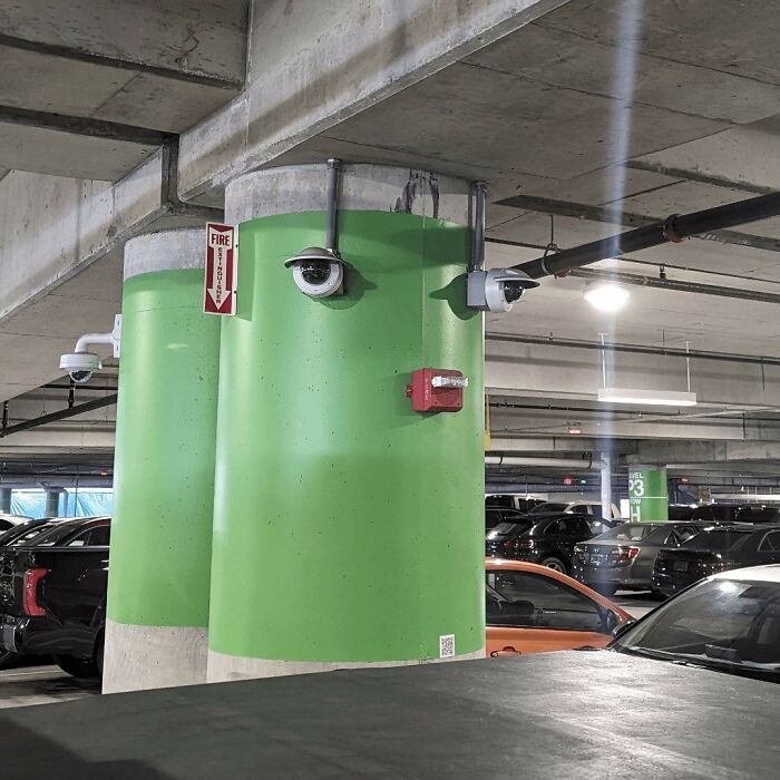A weird image of green parking garage pillars with security cameras arranged like a face, making people go hmmm.