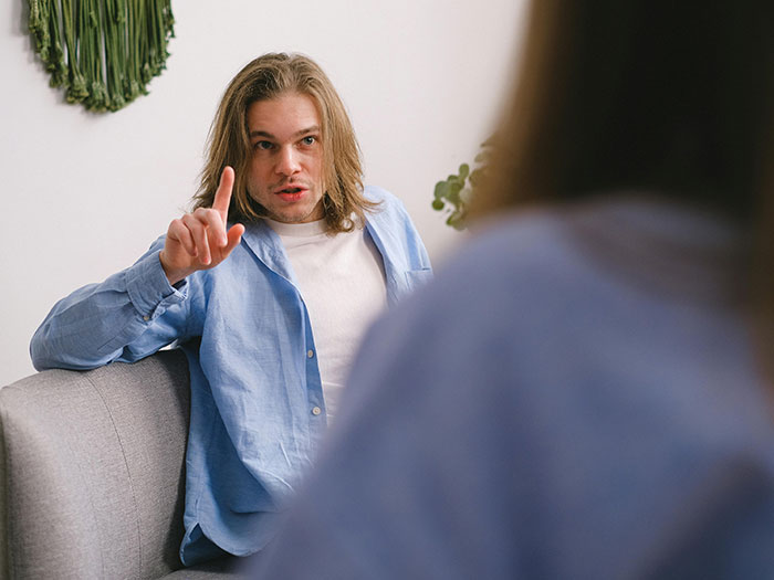 Man with long hair on a first date, pointing and speaking animatedly, perhaps illustrating a horrible first date experience.