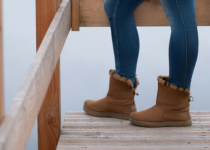 Close-up of person wearing brown boots and blue jeans standing on wooden deck, symbolizing signs economy is struggling.