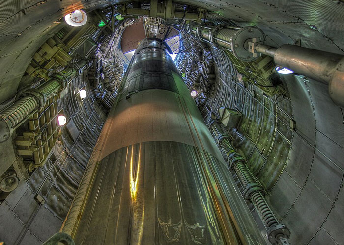 Exclusive access inside a missile silo, showing the massive rocket, structural supports, and lighting from a unique perspective.