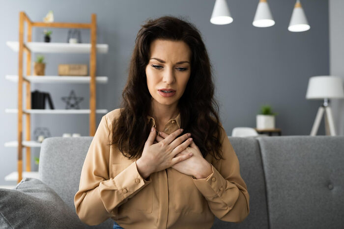 Woman sitting on a couch looking concerned and holding her chest, illustrating random facts about bodies from doctor visits.