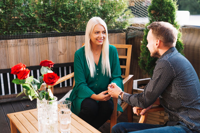 Smiling woman and man holding hands at a patio table with roses, discussing the complexities of friendship betrayals.