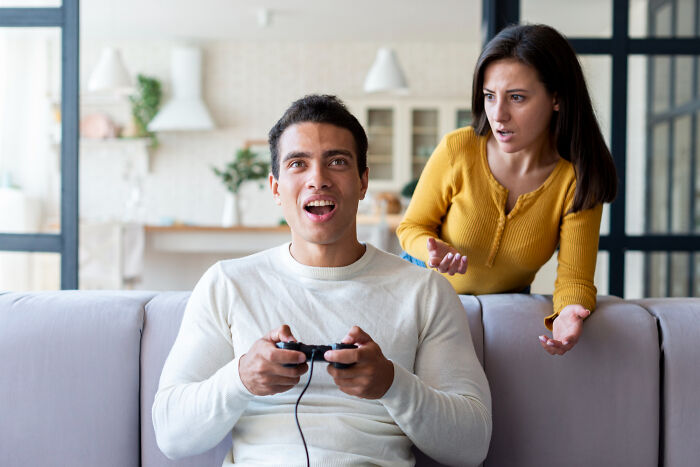 Young man thriving with a video game controller while woman looks upset in a modern living room setting.