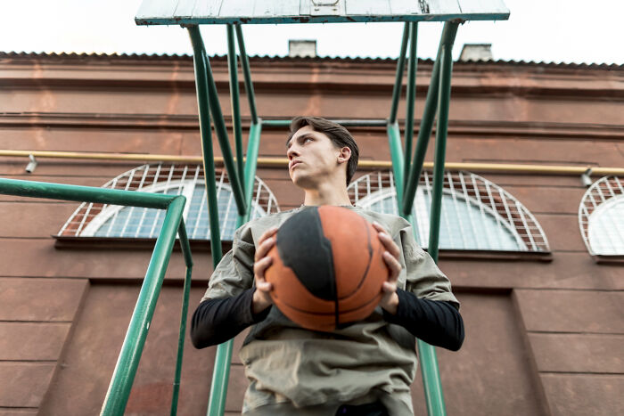 Young man holding a basketball on an outdoor court, illustrating karma comes in all forms and is satisfying.