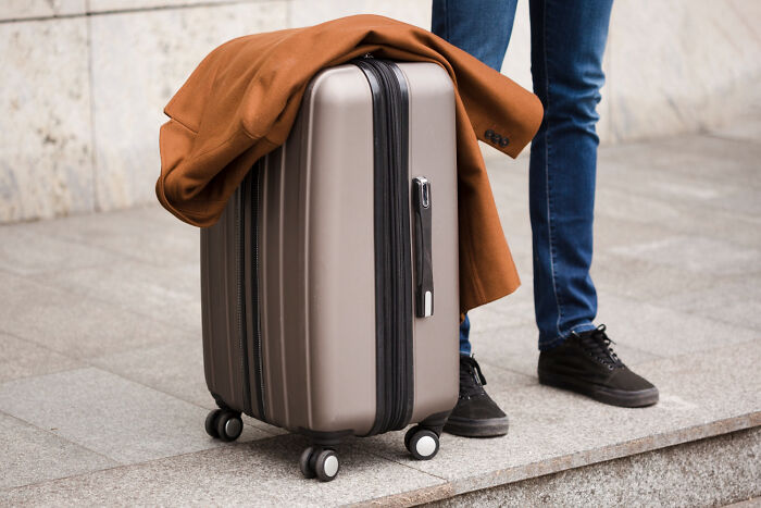 Person standing next to a gray suitcase with a brown coat draped over it, representing TSA confiscated items during travel.