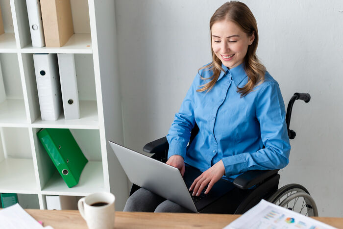 Young woman in a wheelchair working on a laptop, showcasing inspiring comebacks and thriving in a professional setting.